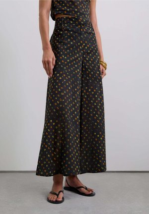 Pantalones de pierna ancha en tela negra con un patrón geométrico en amarillo, naranja y verde; cintura alta, material fluido y un corte relajado.
