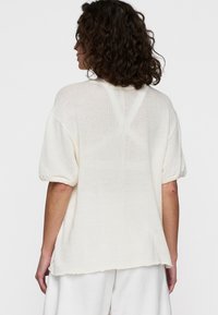 Maglione a maniche corte di un beige chiaro, realizzato in un tessuto a maglia testurizzata, caratterizzato da una vestibilità ampia e un orlo leggermente curvo sul retro.