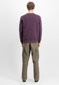 Pulover majica u tamnoljubičastoj pamuku, s rebrastim manžetama i donjim rubom. Uparen s trenirkom u maslinasto zelenoj boji, s velikim bočnim džepovima.