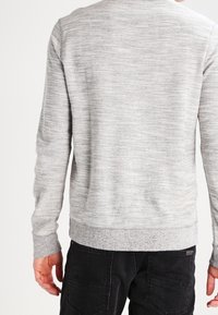 Sudadera gris texturizada con cuello redondo, puños y dobladillo acanalados; presenta un sutil patrón de rayas y un acabado liso en la parte trasera.