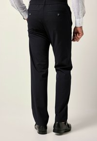 Pantaloni blu navy con vita elastica, tasche posteriori e scarpe nere. Il tessuto è liscio, con una vestibilità sartoriale e una gamba assottigliata.