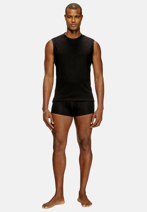 Schwarzes ärmelloses Shirt und schwarze Boxershorts, beide aus glattem Stoff; enganliegendes Design; das Modell steht barfuß vor einem hellen Hintergrund.