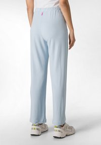 Lichtblauwe broek met een relaxte pasvorm, elastische tailleband en een gladde textuur. Gepaard met beige en grijze sneakers met gele accenten.