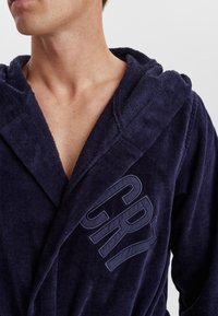 Marineblauer Frottee-Bademantel mit Kapuze und Vordertasche, mit erhabener Schrift "GRY" auf der Brust. Weiche Textur und lässiges Design.