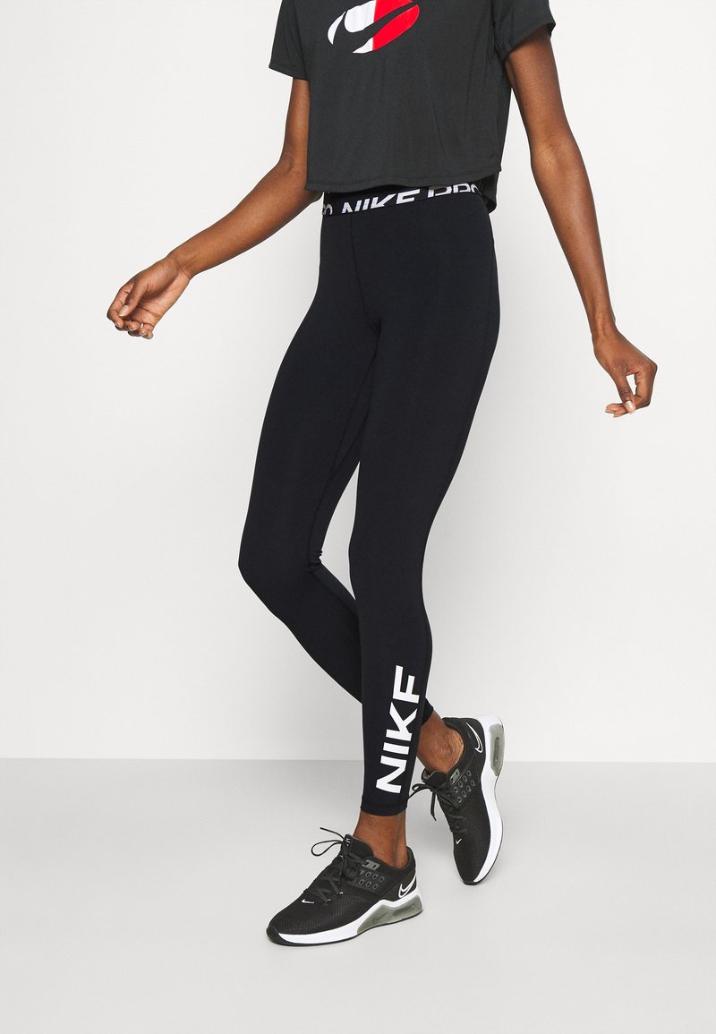 Black stretch leggings with white "NIKE" branding on the lower leg, paired with a black cropped t-shirt featuring a red and white logo.