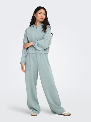 Gaiši zils, kapucis ar rāvējslēdzēju, ar elastīgiem apročiem, kopā ar atbilstošām plašām biksēm. Mīksts audums ar gludu faktūru. Ikdienišķs dizains.