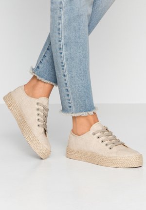 Beige canvas sneakers met geweven jute plateau, ronde neus en grijze veters. Gecombineerd met lichtblauwe jeans met rafelige zoom.