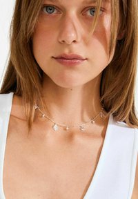 Hõbedast kaelakee erinevate ripatsitega, sealhulgas leht, täht ja pärlivääristused. Lihtne keti kujundus poleeritud viimistlusega.