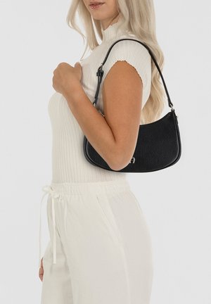 Borsa nera in pelle con superficie texturizzata, forma curva, manico corto e dettagli in metallo dorato, indossata sotto il braccio.