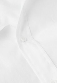 Camisa blanca de botones confeccionada en un tejido ligero, con un cuello clásico, cierre de botones y una textura mínima con sutiles detalles de costura.