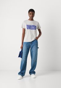Gray cotton t-shirt with blue graphic text, paired with light blue wide-leg jeans. Accessories include a small blue handbag and white sneakers.