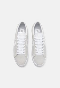 Scarpe da ginnastica in camoscio grigio con lacci bianchi e suole in gomma. I lati presentano un logo semplice e perforazioni per la traspirabilità.