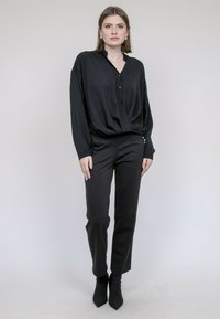 Chemise noire à manches longues avec un devant boutonné et un col, associée à un pantalon noir ajusté et des bottines. Texture lisse dans l'ensemble.