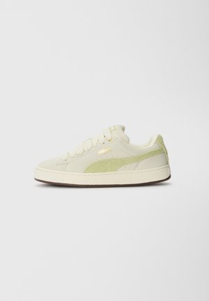 Cream canvas sneakers with green suede accents, round toe, flat laces, gold branding, and a textured rubber sole.