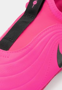 Chaussure de sport rose avec une tige en synthétique texturé, présentant une sangle noire et un logo swoosh noir proéminent sur le côté.