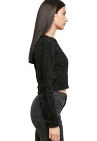 Maglione nero accorciato in materiale morbido con maniche lunghe, abbinato a jeans neri a vita alta, che mostrano una vista laterale.