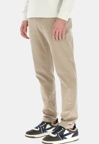 Chino beige con una vestibilità dritta, caratterizzati da una trama liscia. Indossati con sneakers scure con dettagli bianchi e blu.