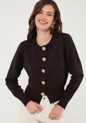 Black cardigan with long sleeves, round neckline, and gold flower-shaped buttons down the front. Tailored fit, smooth texture.