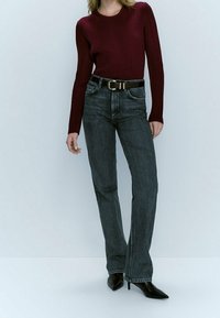Jean taille haute gris foncé, ajusté avec une coupe bootcut, associé à un haut bordeaux à manches longues côtelé et une ceinture noire.