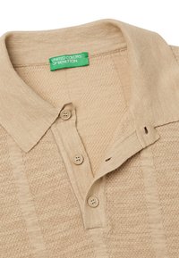 Beige polo shirt with a textured pattern, two buttons at the collar, and a green label reading "UNITED COLORS OF BENETTON" on the inside.