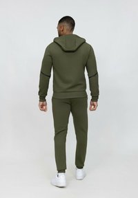 Un sweat à capuche vert olive et un pantalon de jogging assorti, avec des poignets et un ourlet côtelés, des bandes noires en accent, associés à des baskets blanches.