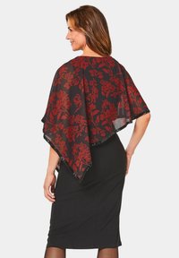 Zijdeachtige zwarte sjaal met een rood bloemenpatroon en paillettenrand, over een getailleerde zwarte jurk gedrapeerd. Stof is lichtgewicht met een zachte textuur.