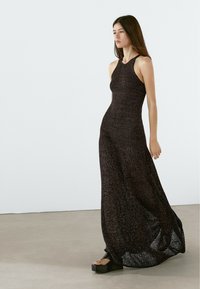 Abito lungo nero senza maniche realizzato in un materiale a maglia testurizzata, con un corpetto aderente e un leggero svaso all'orlo; indossato con sandali platform spessi.