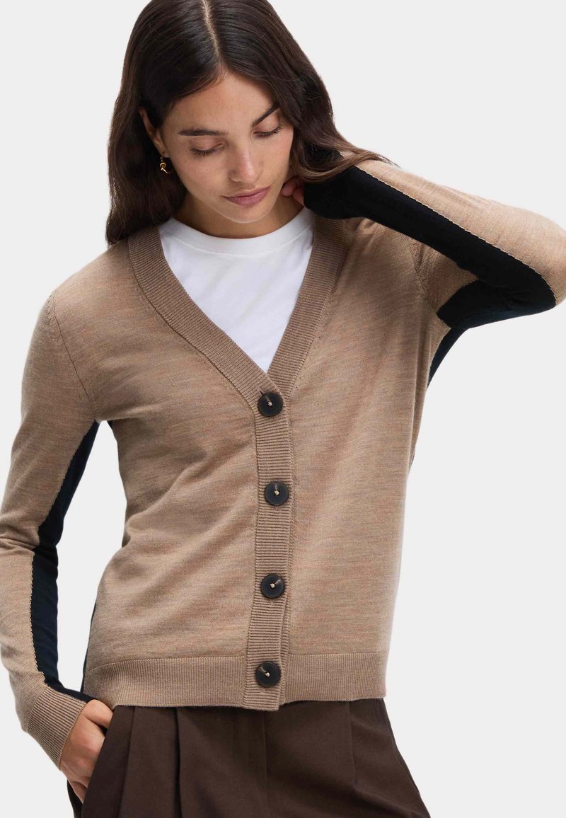 Beige kardiagan med svarta stickade detaljer, med v-ringning, långa ärmar och fem mörka knappar fram. Slät textur och figurnära design.