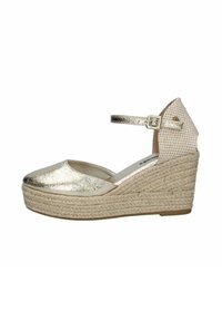 Espadrilles de cuña metálica dorada con suela de yute trenzado, correa en el tobillo y acento de tela a rayas en la parte posterior. Textura suave y diseño de punta redonda.