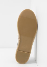 Semelle d'une chaussure avec une base en caoutchouc texturé de couleur beige, présentant un bord duveteux de couleur claire et une section supérieure lisse de couleur noire.