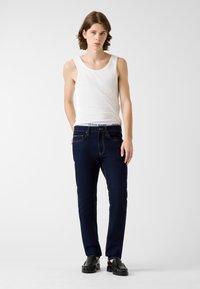 Jeans blu navy a taglio slim, con tessuto texturizzato, design a cinque tasche e cuciture a contrasto; abbinati a una canotta bianca.