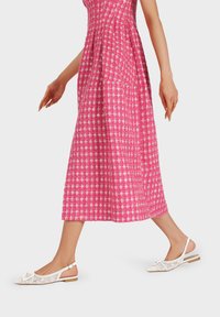 Abito midi a quadri rosa con plissettature, abbinato a scarpe slingback bianche con motivo testurizzato e tacco basso.