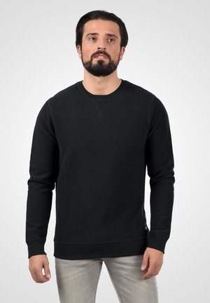 Must must have pikaa varrukatega, ümar kaelus, soonikkoes varrukates ja allääris; pehme tekstuur, millel on õrn muster, kantud heledate hallide teksade kohal.