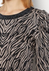 Pullover lavorato a maglia nero e beige con motivo a strisce zebra e fili metallici, caratterizzato da un collo a coste e maniche voluminose.