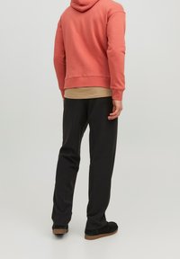 Sudadera con capucha en color coral, mezcla de algodón, con un bolsillo tipo canguro. Combinada con pantalones negros ajustados y calzado negro con suelas marrones.