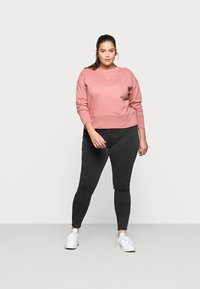 Pink cropped sweatshirt with long sleeves, paired with black skinny jeans and white sneakers. Smooth texture, relaxed fit, and simple design.