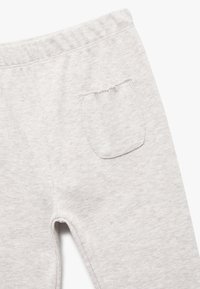 Grijze gebreide trainingsbroek met een elastische tailleband en een enkele achterzak met een rafelige rand, wat de zachte, gemêleerde stof benadrukt.