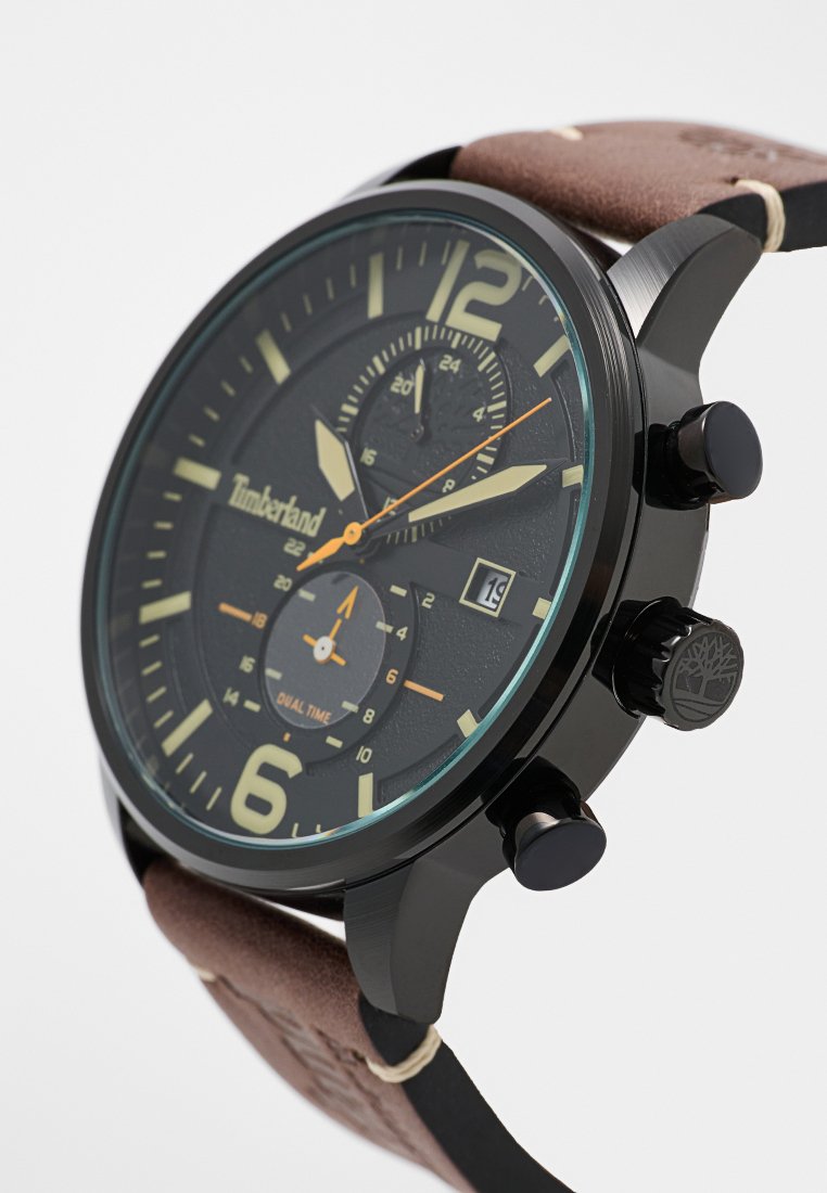 Reloj analógico negro con una esfera oscura texturizada, acentos plateados, correa de cuero marrón y tres subesferas, que incluyen un indicador de fecha.