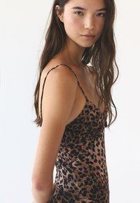 Leopardprint satijnen jurk met dunne bandjes, met een aansluitende pasvorm en een zachte textuur. Het patroon bestaat uit donkere vlekken op een lichte achtergrond.