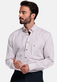 Langsliepend overhemd met lange mouwen in het wit met een rood en blauw ruitpatroon. Bevat een kraag, een borstzak en zwarte knopen.