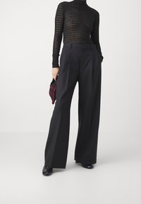 Haut noir ajusté à manches longues avec un motif en tricot ouvert texturé, associé à un pantalon noir taille haute à jambes larges.