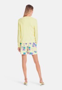 Yellow long-sleeve top paired with floral-patterned shorts featuring purple and green hues, displaying a relaxed fit and soft texture.