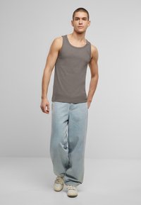 Grå bomullstopp med ribbet tekstur, kombinert med løse lyseblå jeans og hvite joggesko. Modellen står foran en nøytral bakgrunn.