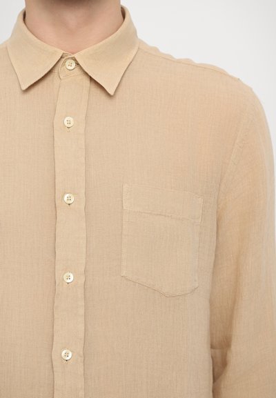 Camicia button-up color beige chiaro, con colletto, tessuto testurizzato, una tasca sul petto e sette bottoni lungo la parte anteriore.