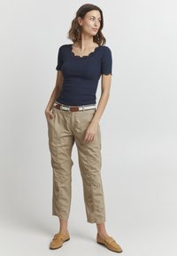 Haut à manches courtes marine avec finition en dentelle, associé à un pantalon cargo beige clair avec poches, porté avec une ceinture marron et des chaussures à enfiler beige.