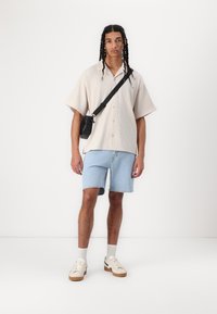 Short-sleeve beige striped shirt, light blue denim shorts, black crossbody bag, white sneakers with beige soles, gray crew socks.