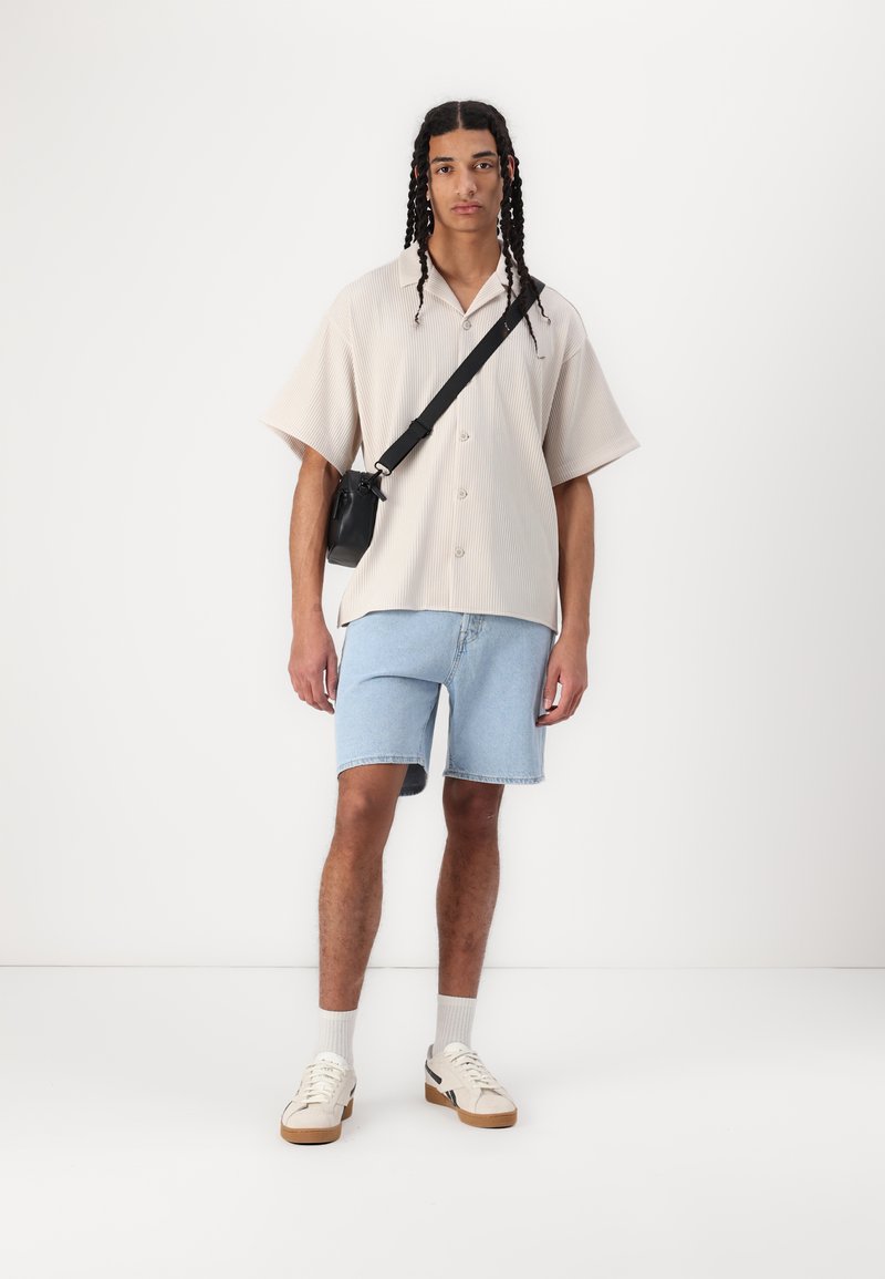 Krótki beżowy koszulka w paski, jasnoniebieskie szorty dżinsowe, czarna torba na ramię, białe sneakersy z beżowymi podeszwami, szare skarpetki za kostkę.