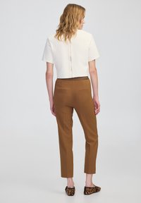 Weißes, kurzes Oberteil mit kurzen Ärmeln und Reißverschluss auf der Rückseite; braune, taillierte Hose im Slim-Fit mit Gesäßtaschen; Loafers mit Animal-Print.