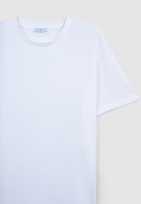 Camicetta bianca a maniche corte realizzata in tessuto texturizzato con colletto rotondo e un'etichetta interna, caratterizzata da un sottile motivo a righe.