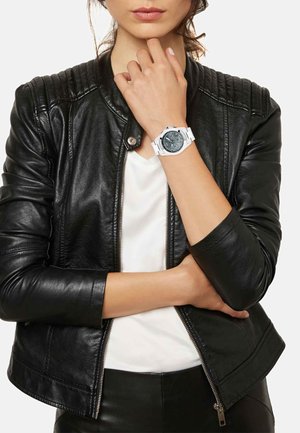 Hvidt ur med en rund grå urskive, sølv detaljer og gummirem båret på et håndled. Sort læderjakke med quiltede skuldre.